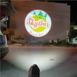 Logo SkyBar Beach Bar được chiếu lên tường ngoài của một toà nhà vào ban đêm, đèn chiếu đặt dưới đất phía trước