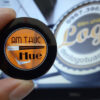 Bàn tay cầm một lăng kính tròn in logo Ẩm Thực Huế nền cam, phía sau là màn hình máy tính hiện logo Đèn chiếu Logo